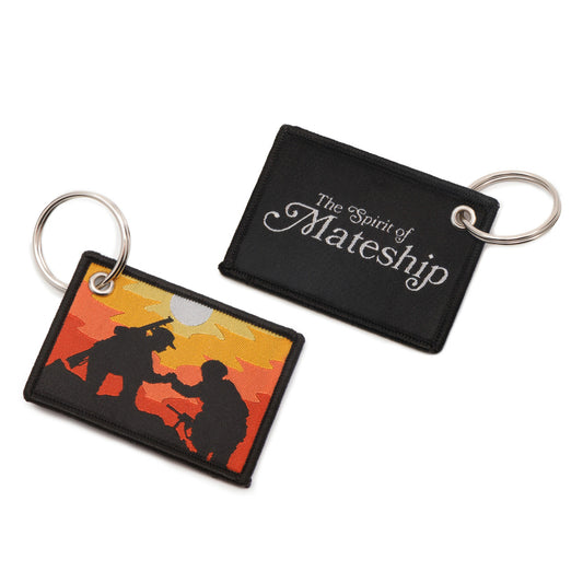 The front of the key tag features a striking image against the backdrop of a mesmerizing sunset. Here, you'll find a poignant silhouette: a WW1 digger extending a helping hand to a modern Australian soldier, both navigating a muddy battlefield. This symbolic representation speaks volumes about the unbreakable bond forged through adversity. www.defenceqstore.com.au